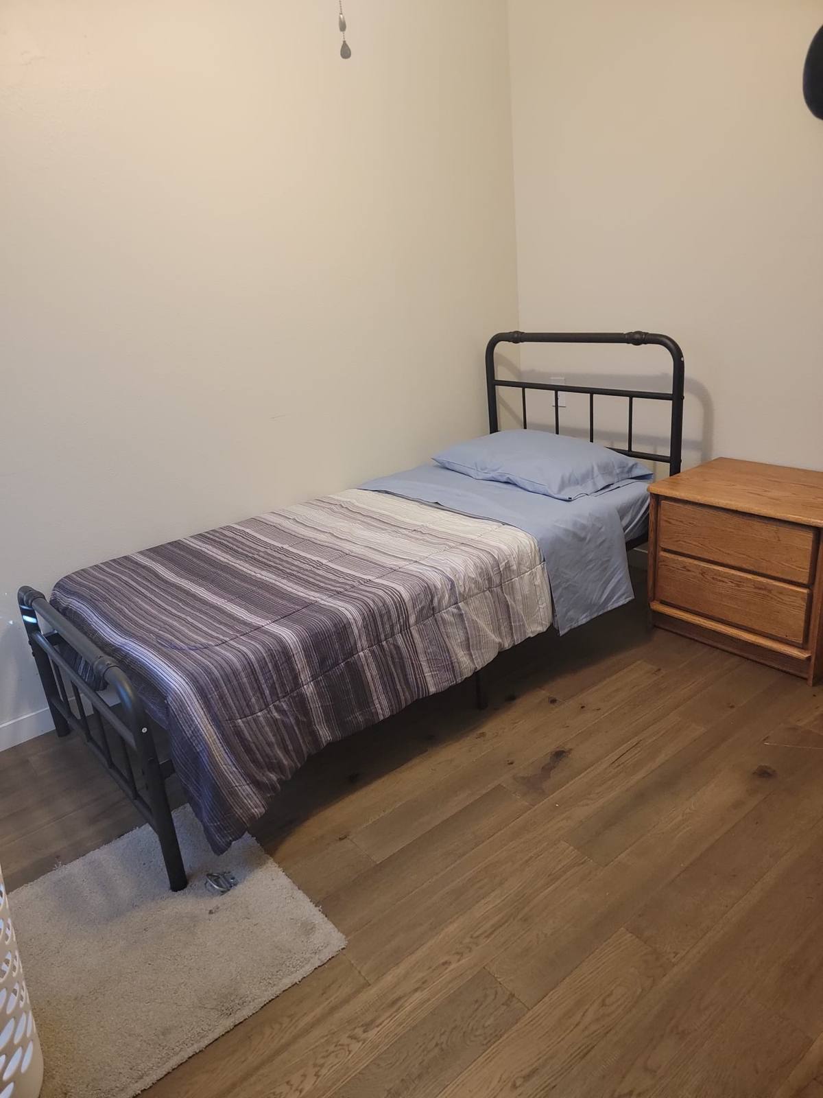 A resident bedroom with a single bed, blue sheets and a wooden nightstand.