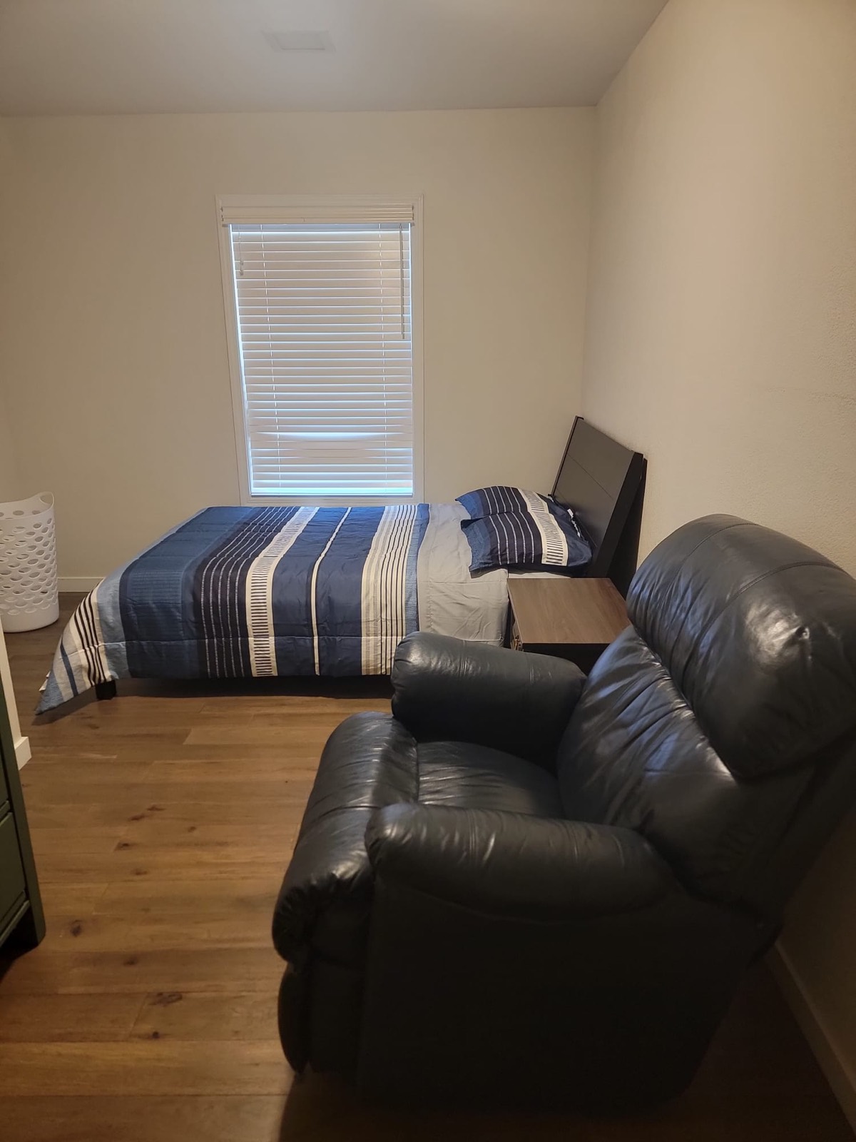 A second resident bedroom with a bed under the window, a nightstand and a leather recliner.
