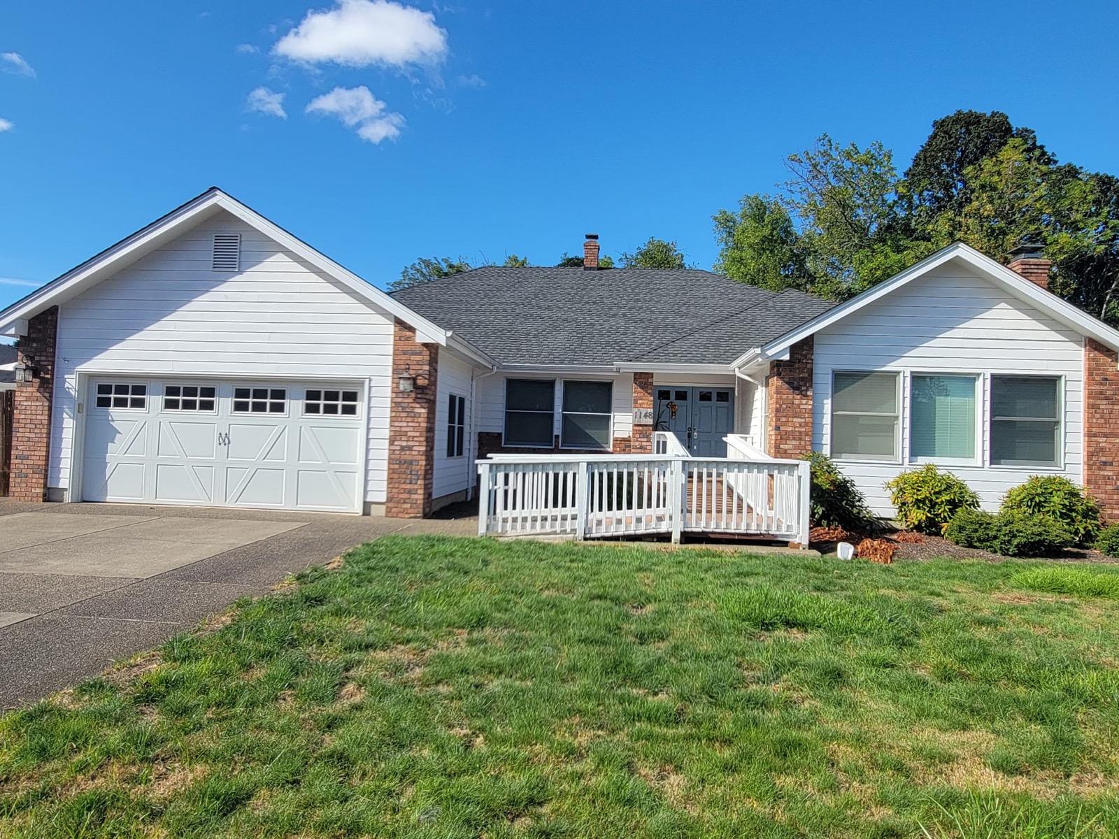 Angled view of the single-storey home showing the driveway, garage, front lawn and mature trees behind the house.