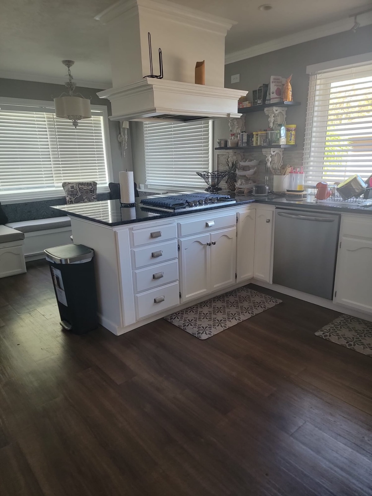 The kitchen, with white cabinets, a dark stone counter and a gas hob, beside a sunny window seat.