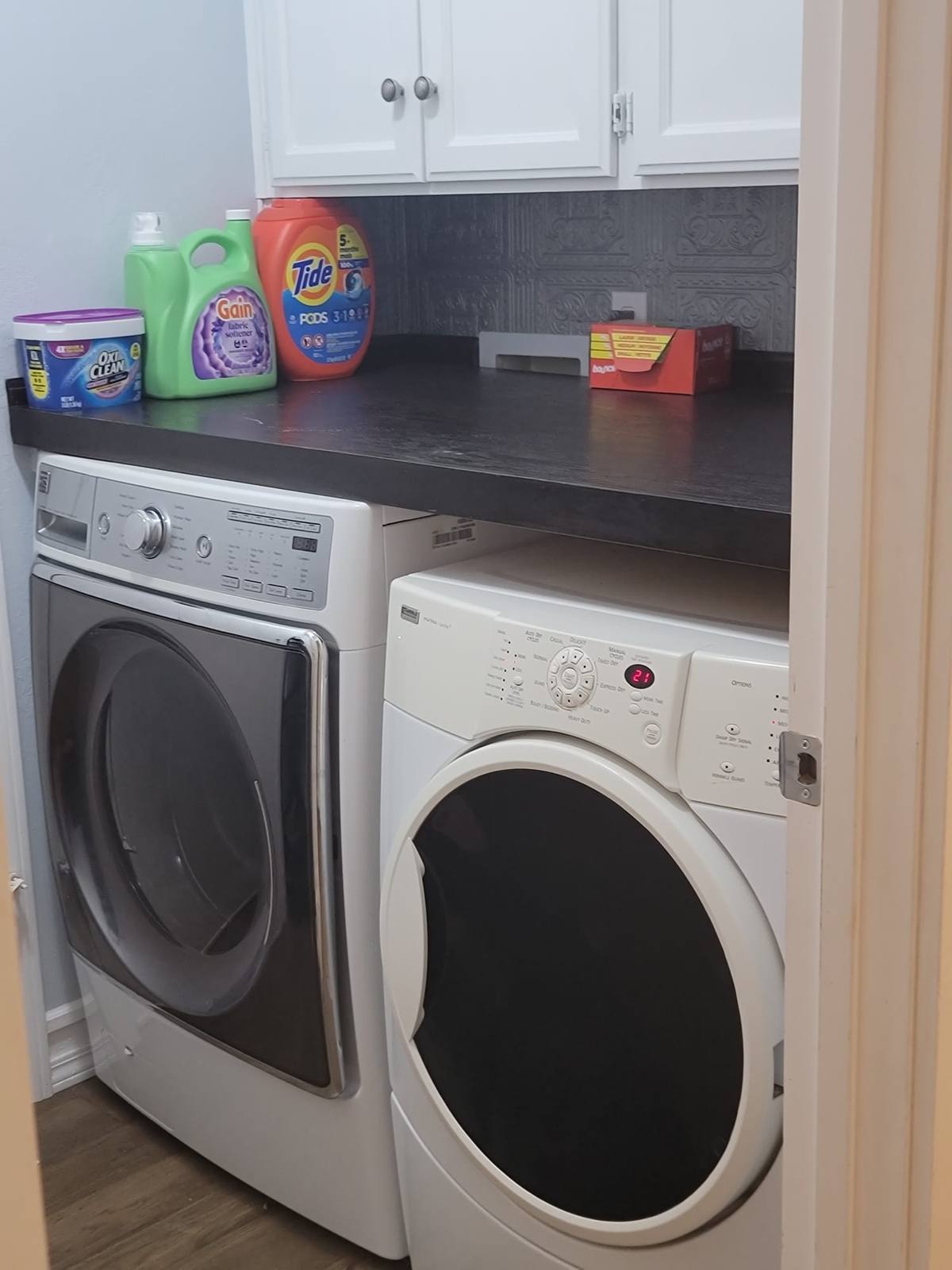 The laundry room, with a front-loading washer and dryer under a counter and cupboards.