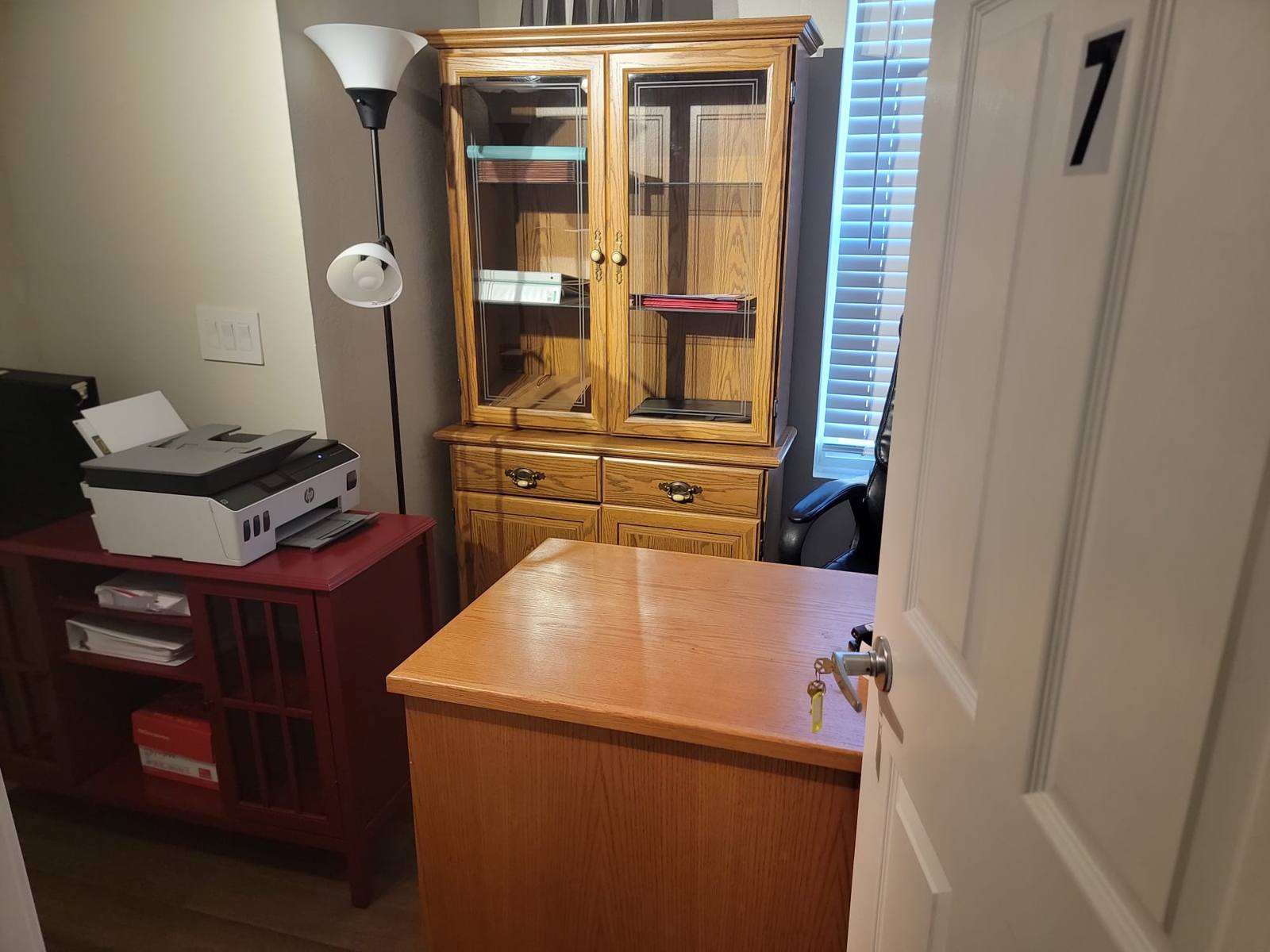 The office, with a wooden desk, a glass-fronted cabinet and a printer.