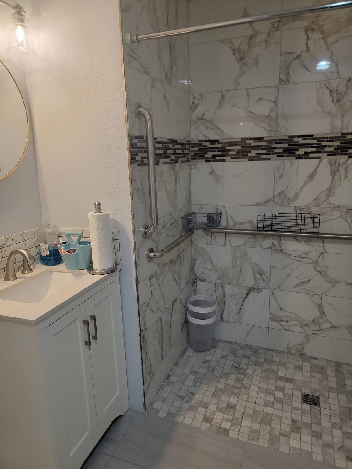 A walk-in shower with grab bars and a level tiled floor, beside a vanity sink.