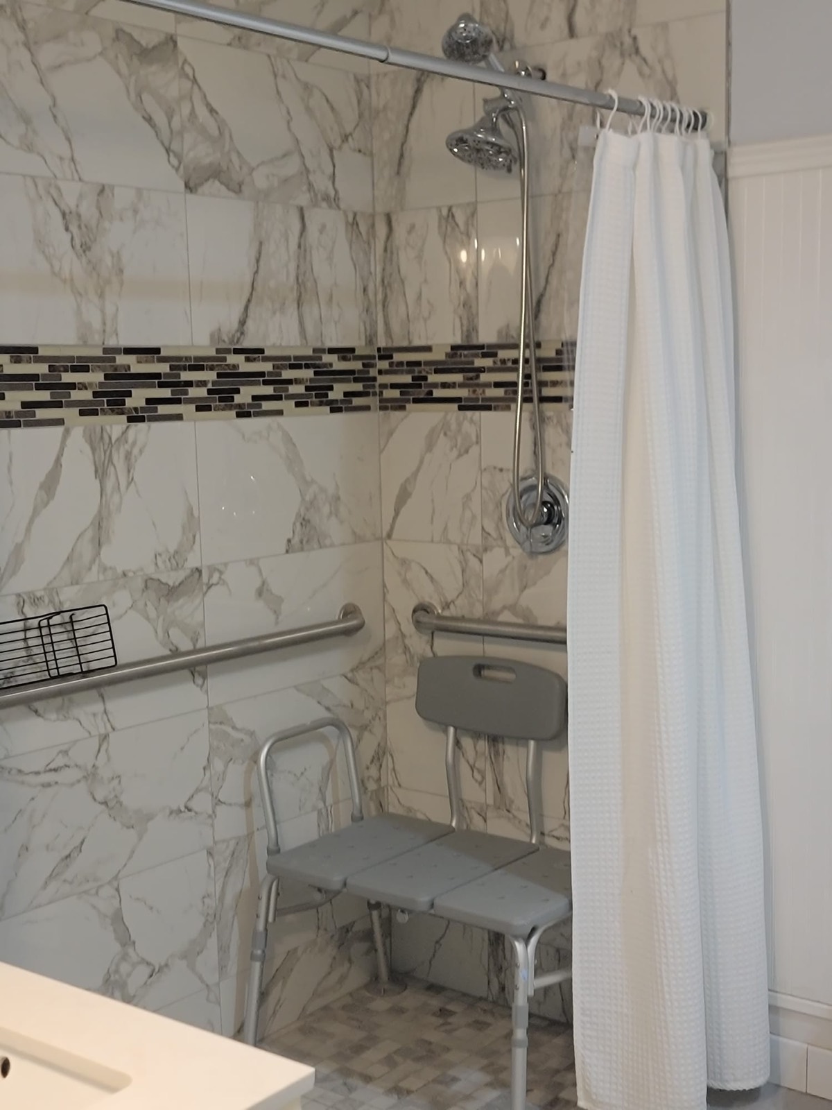 A tiled walk-in shower with grab bars on the walls and a shower transfer bench.